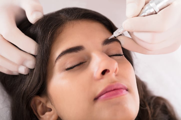 Cosmetologist Applying Permanent Make Up On Woman's Eyebrows In Beauty Spa